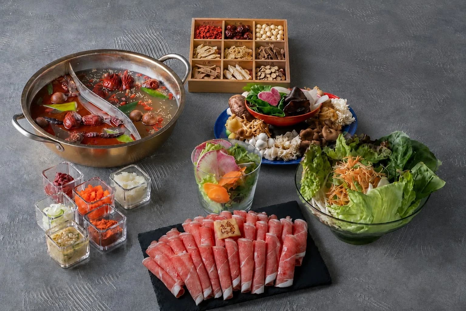 黒い天板に麻辣湯と白湯の二色鍋、山型に積んだロールラム、野菜ときのこの大皿、ラムチョップを並べたコースの全景
