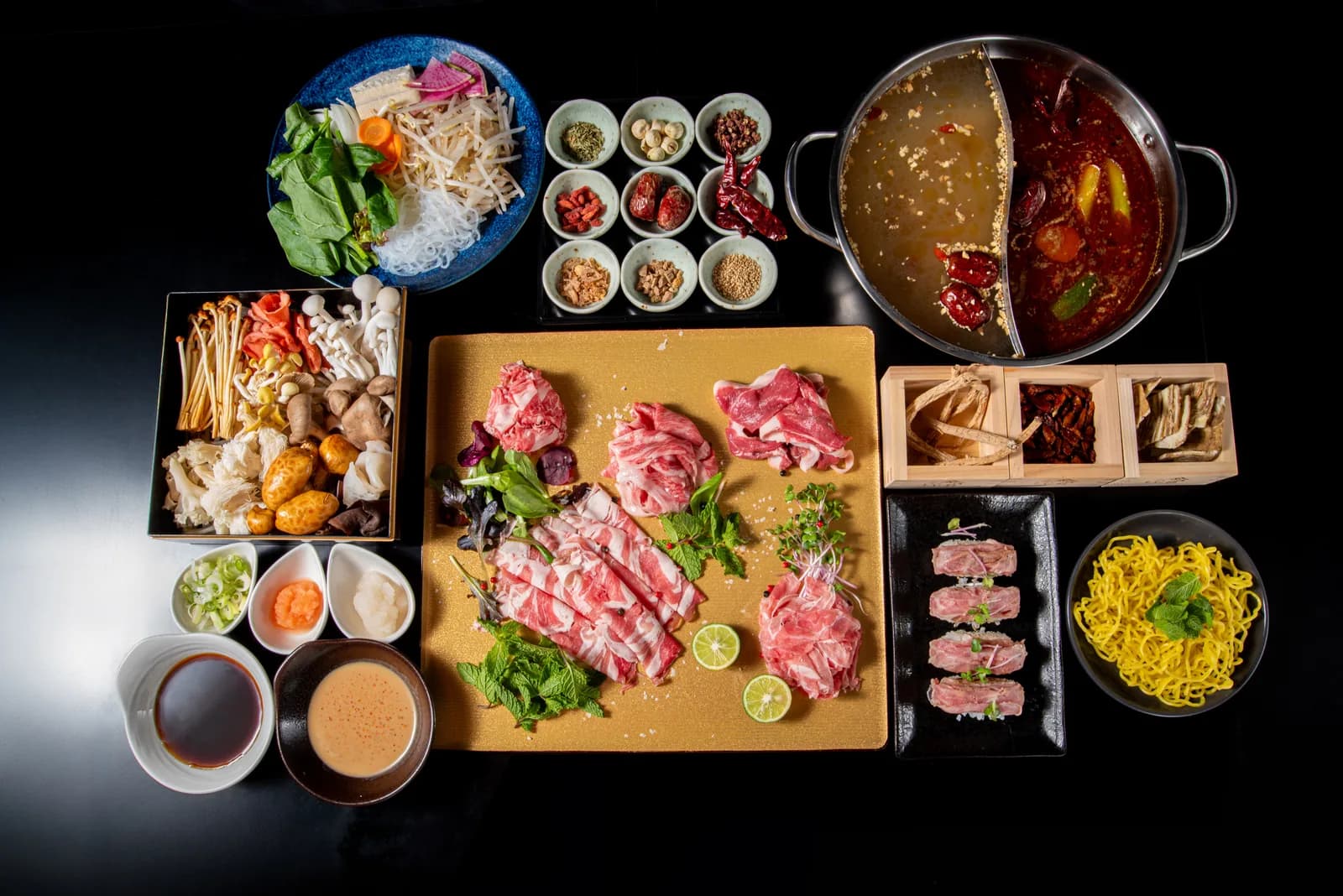 コース全景の真俯瞰。麻辣湯と白湯の二色鍋を右上に、金の板の肉、薬味九種、きのこ重箱、たまご麺が囲む