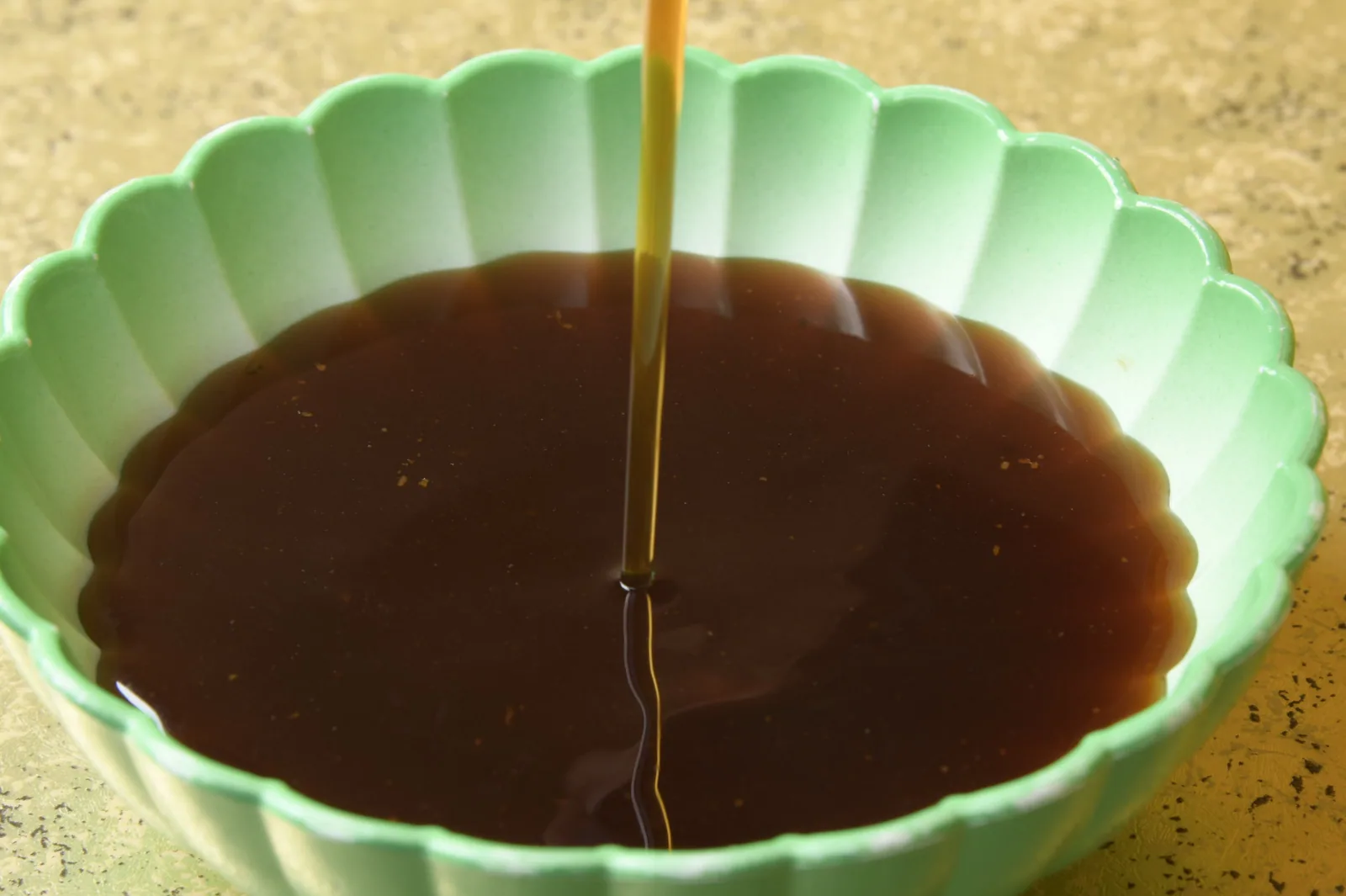 淡緑の輪花鉢に注がれる謹製だれ。醤油ベースの濃い赤褐色の澄んだたれに、細い一筋が落ちて輪が広がる
