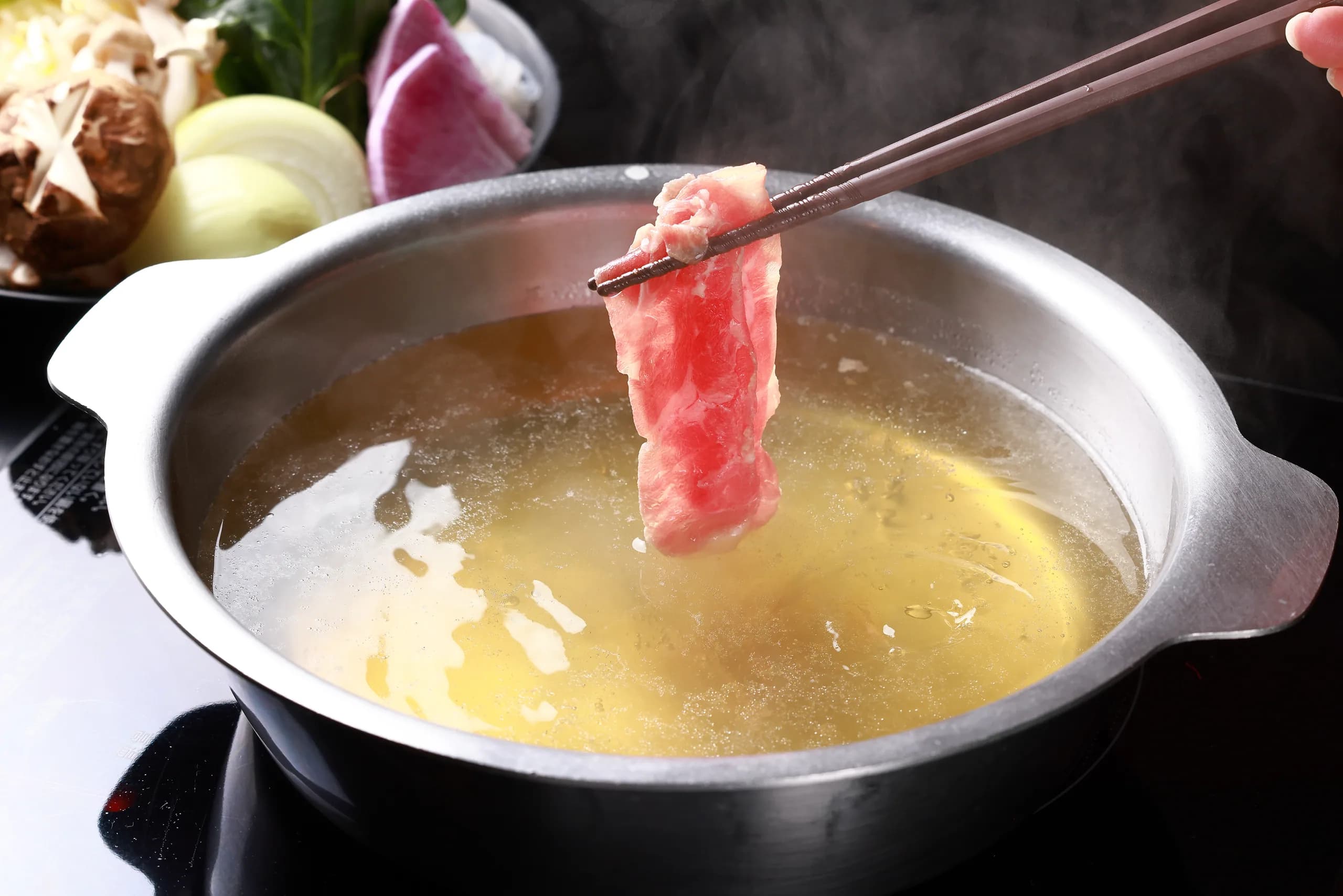薄切りの吟醸ラムを箸で持ち、白湯の鍋の上でくぐらせるところ。奥に高原野菜と椎茸が控える