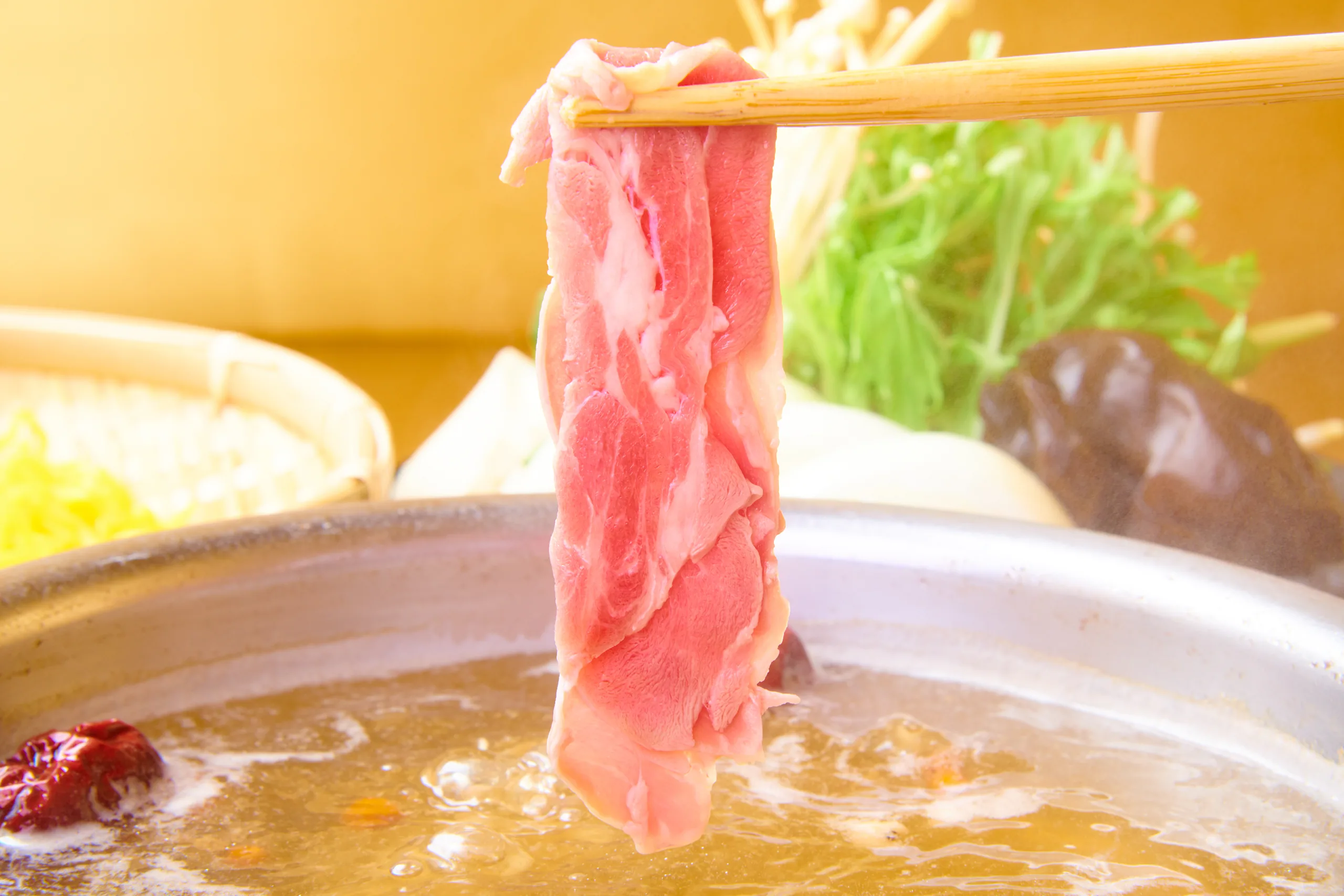 箸で持ち上げた薄切りの吟醸ラムが、白湯の鍋の上で湯気に包まれる。奥に高原野菜と椎茸が控える