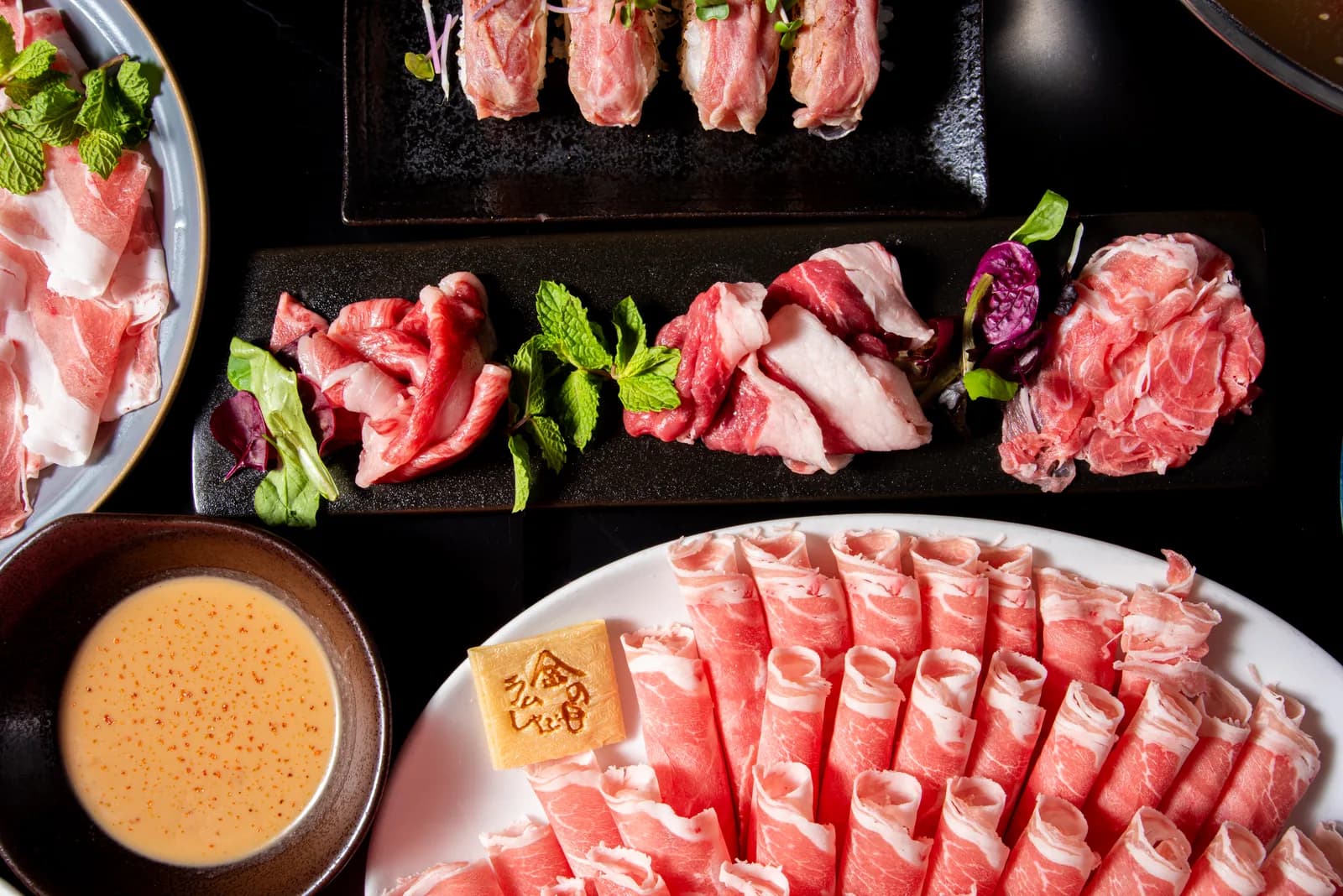 黒いスレートに数種のラム肉を一列に並べた斜俯瞰。手前に「金の目」の焼印プレートとロールラムの大皿