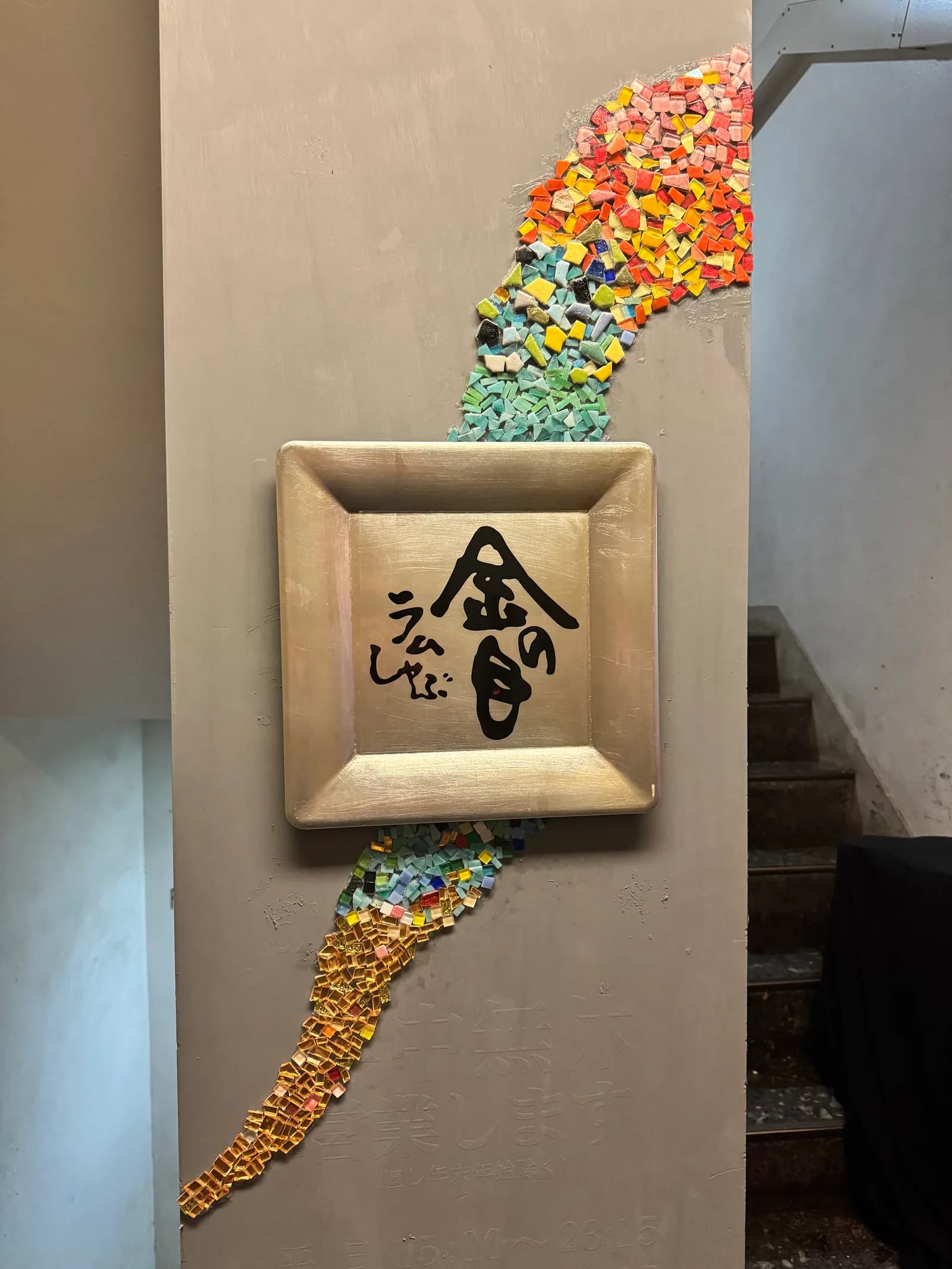 銀座本店の入口に掛かる木枠の看板。「金の目」の墨字を囲むように、色ガラスと金箔のモザイクが壁を走る