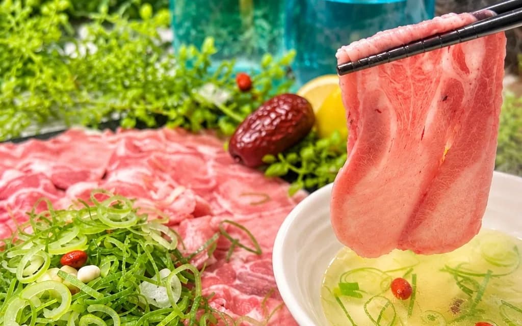 用筷子夾起薄切羊肉,正要放入漂著蔥花和枸杞的白湯沾碗,後方是大盤羊肉