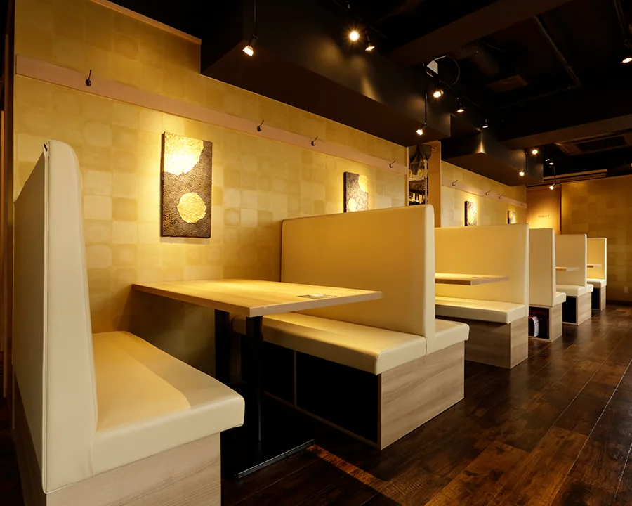 池袋店的卡座。金色棋盤格牆面上等間距掛有金色藝術畫板,奶油色長椅與木桌並排