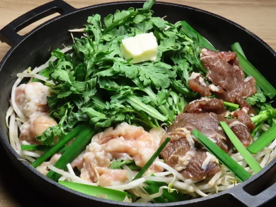 铁锅中备好的烹调前羊内脏火锅。豆芽上摆放羊内脏与调味羊肉、茼蒿、韭菜,中央放黄油
