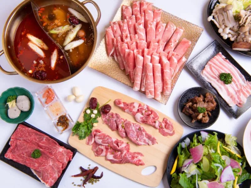 白色背景上排开的整套套餐俯拍。金色鸳鸯锅、薄切羊肉、羊排、生羊肉、内脏、菌菇、沙拉