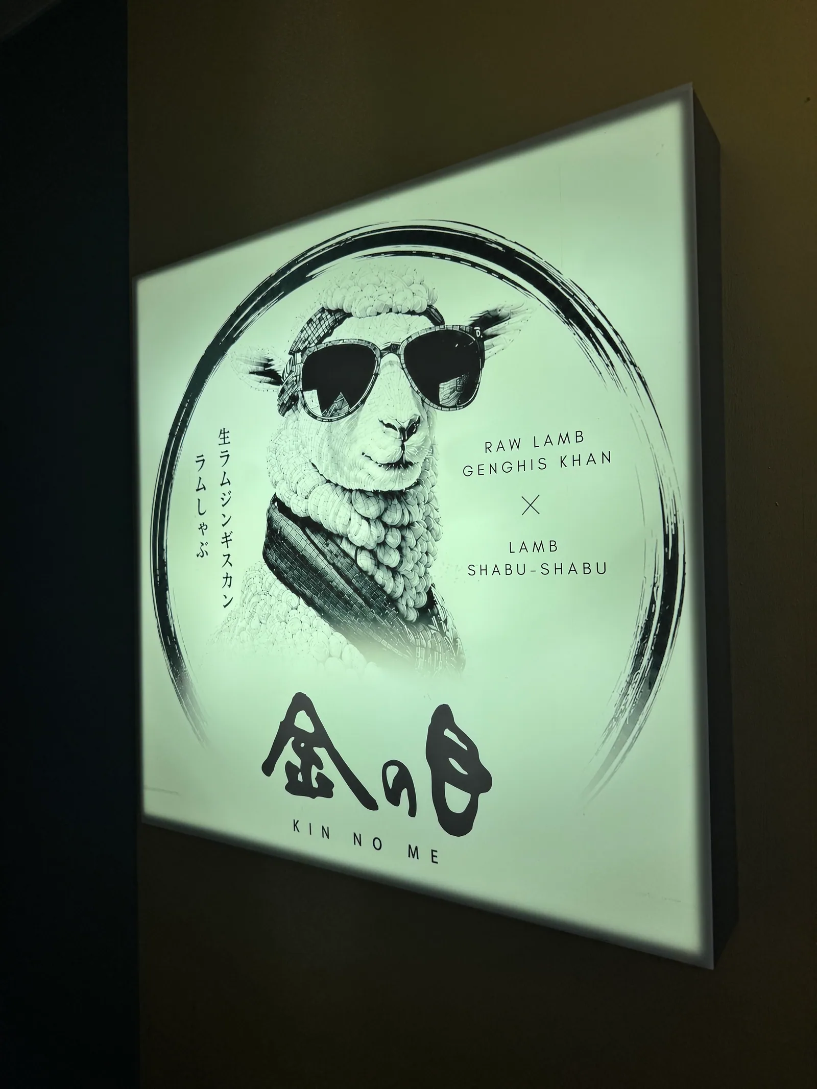 渋谷店の入口に灯る円形サイン。サングラスをかけた羊の意匠と「金の目」の墨字が浮かぶ