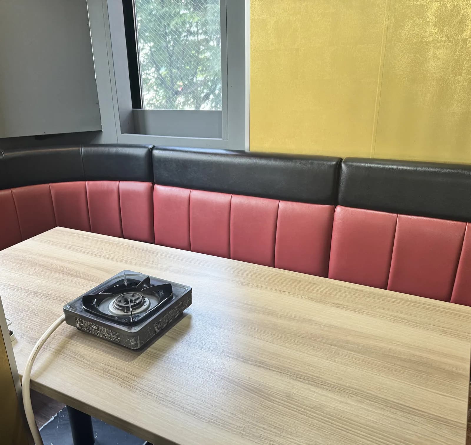 新宿店靠窗的卡座。红黑两色沙发沿金箔质感的墙面环绕,木桌上放着卡式炉