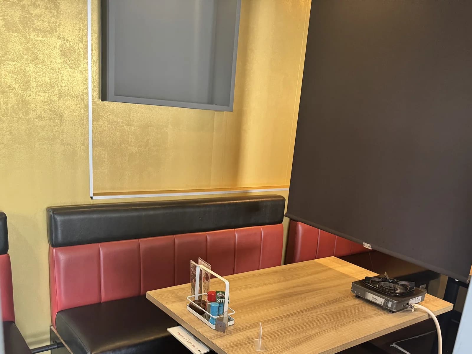新宿店的卡座。红黑两色沙发背靠金箔质感的墙面围着木桌,右侧以黑色卷帘隔开